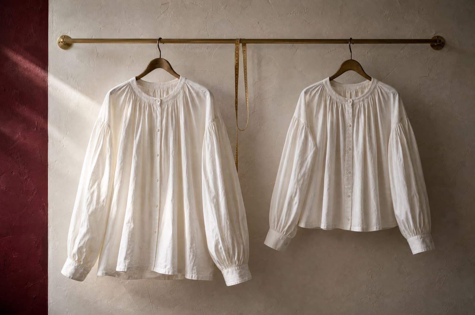 The same blouse in two sizes hung side by side on one rail, with a measuring tape between them.