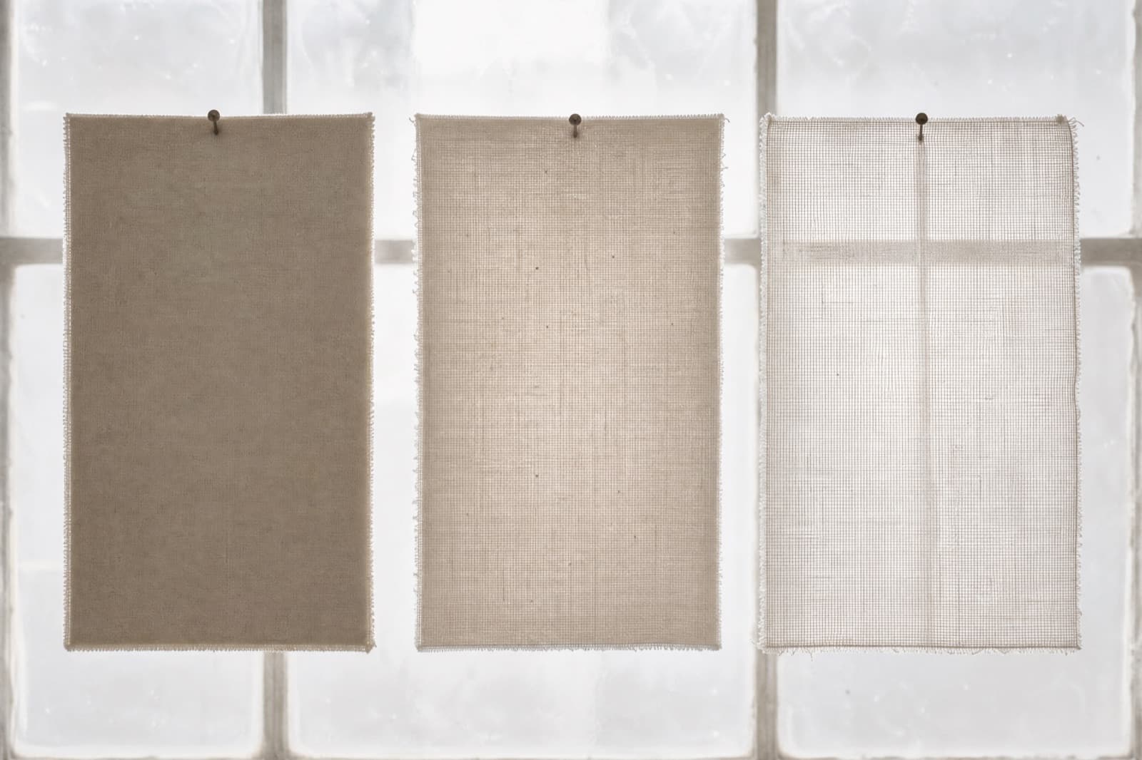 Three swatches of pale cloth pinned against a bright window, showing opaque, semi-sheer and sheer side by side.